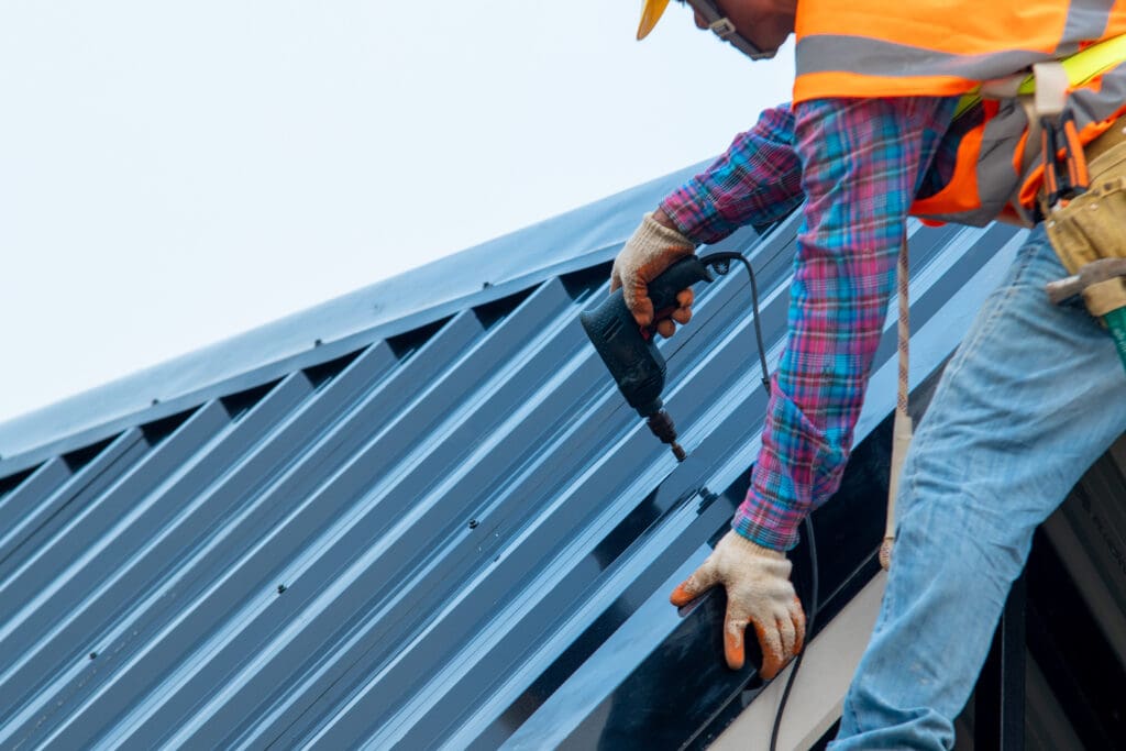 commercial roof maintenance Construction worker wearing safety harness belt during working on roof structure of building on construction site,Roofer using air or pneumatic nail gun and installing metal roof tile on top new roof.