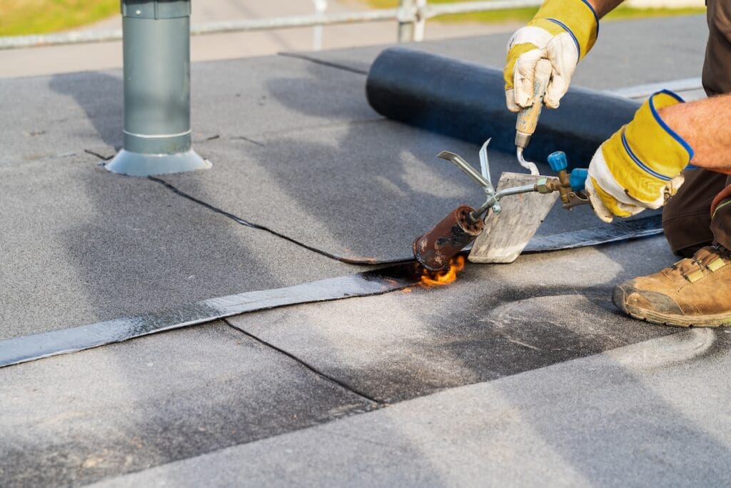 Man Heating and melting bitumen roofing Flat roof installation.