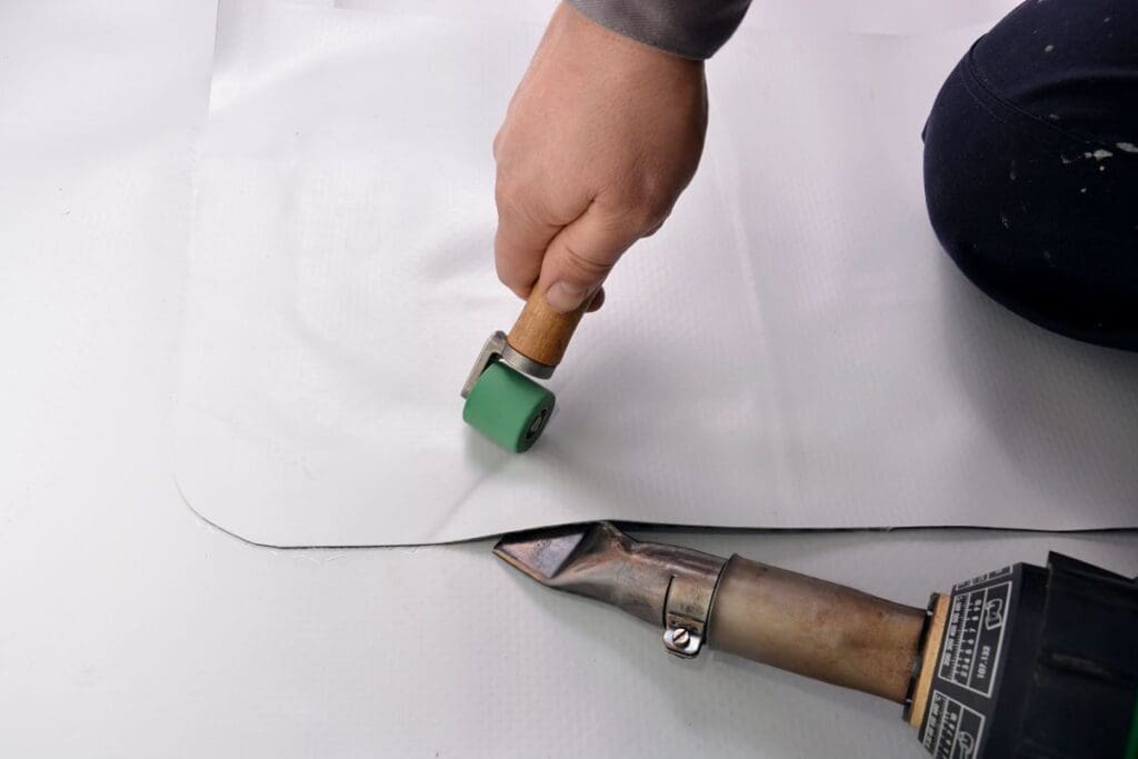 roofing membrane worker installing TPO using heat gun and roller