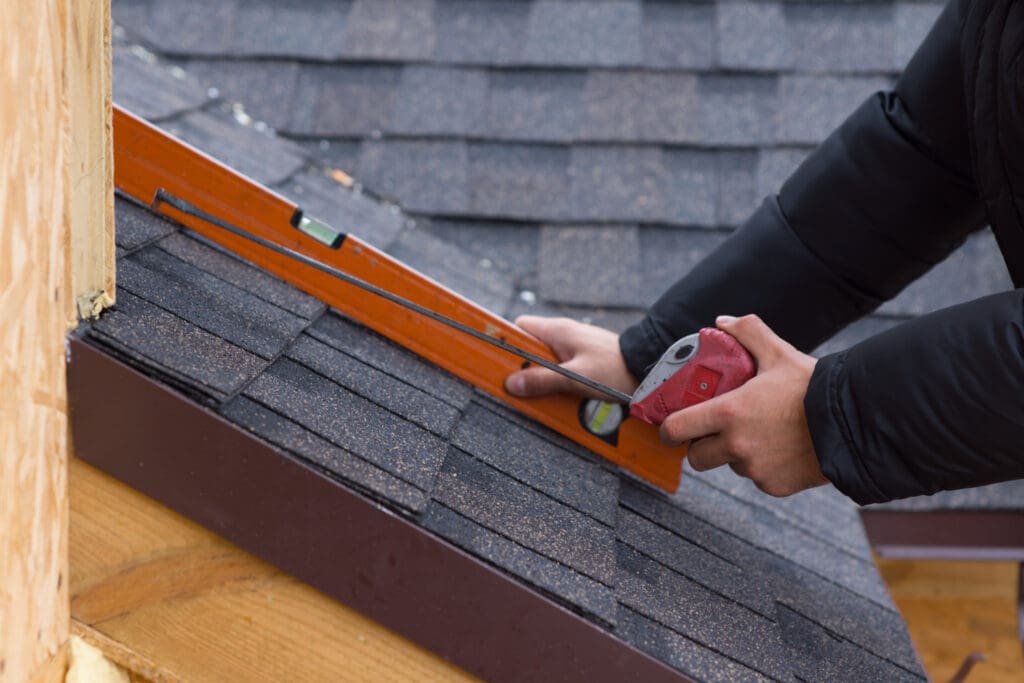 low slope roof pitch Roofer holding a tape measure and spirit level in his hands over newly installed tiles on a new build wooden house
