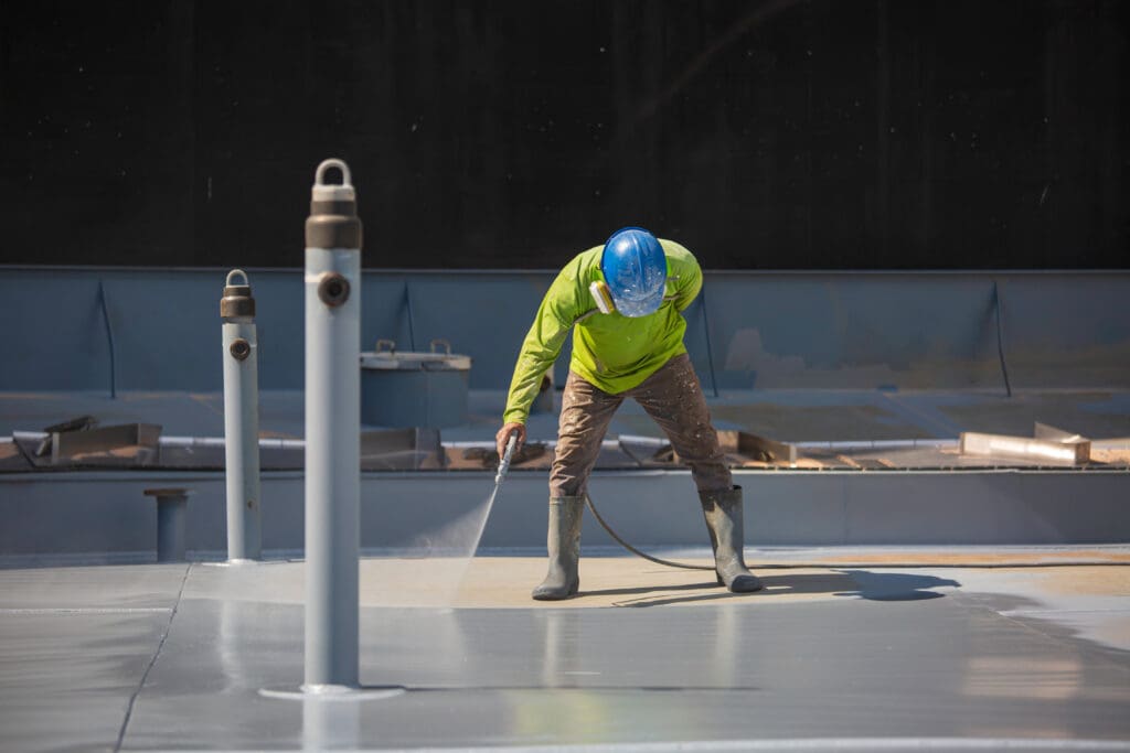 commercial roof coating cost worker applying coat using hose