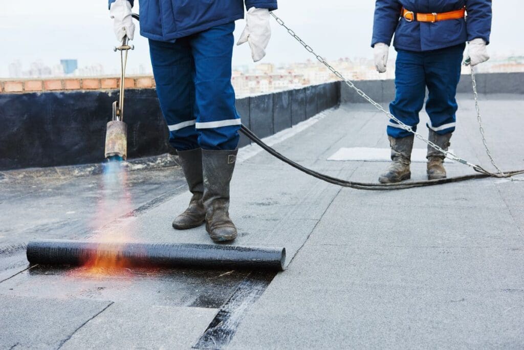 built up roofing system workers applying layer of bitumen