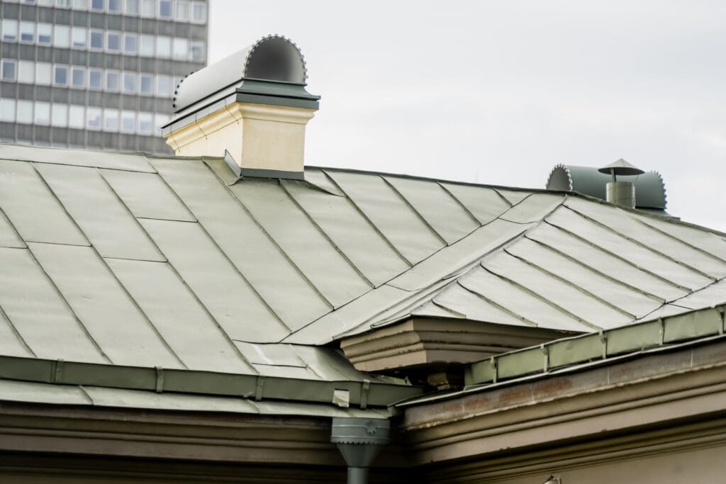 Green painted standing seam metal roofing system featuring rendered stucco chimney stacks with decorative arched metal cowls