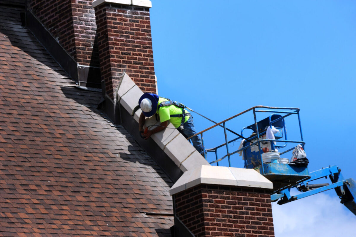 Construction worker uses sander in the repair of stonework on an historic church in Arkansas. He is standing on a lift and working on the roofline.