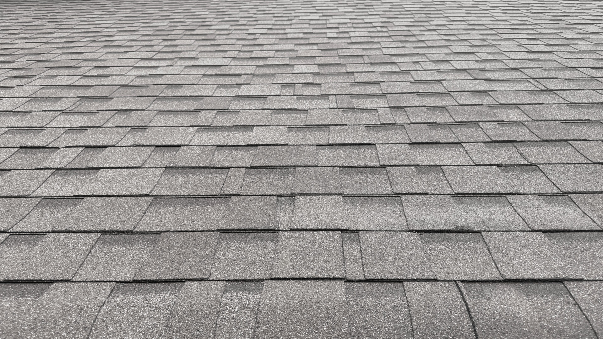 A close-up view of a gray asphalt shingle roof, showing the repeating rectangular pattern and textured surface from a low angle.