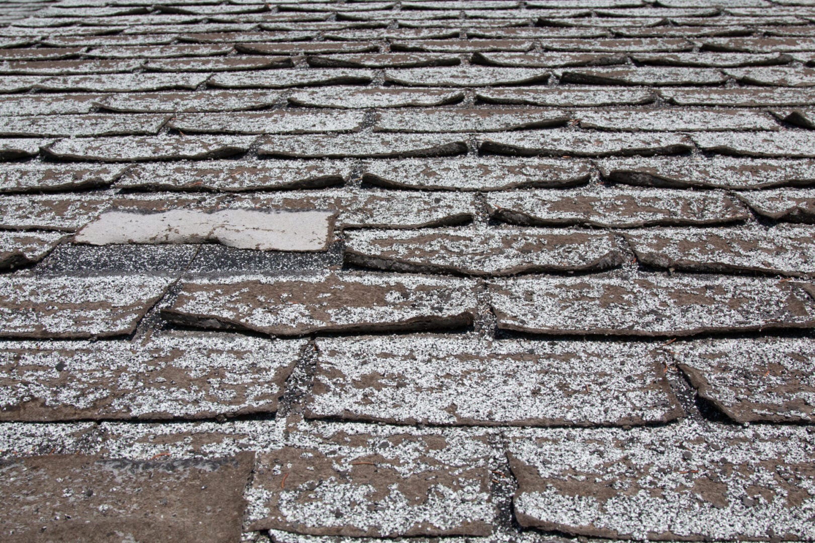 Old worn out asphalt shingles on the roof of a residential home.