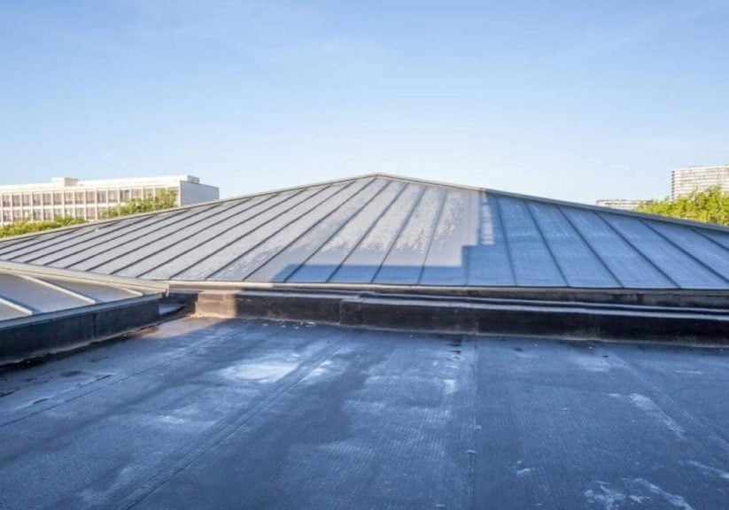 Low-slope metal roof with standing seams on a commercial building, featuring skylights and flat roofing