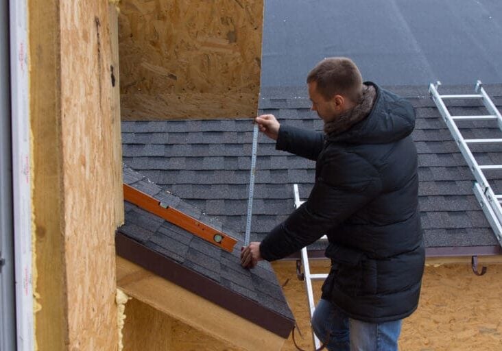 low slope roof pitch Roofer measuring tiles on a new house with a tape measure as he stands on a ladder while installing the roof