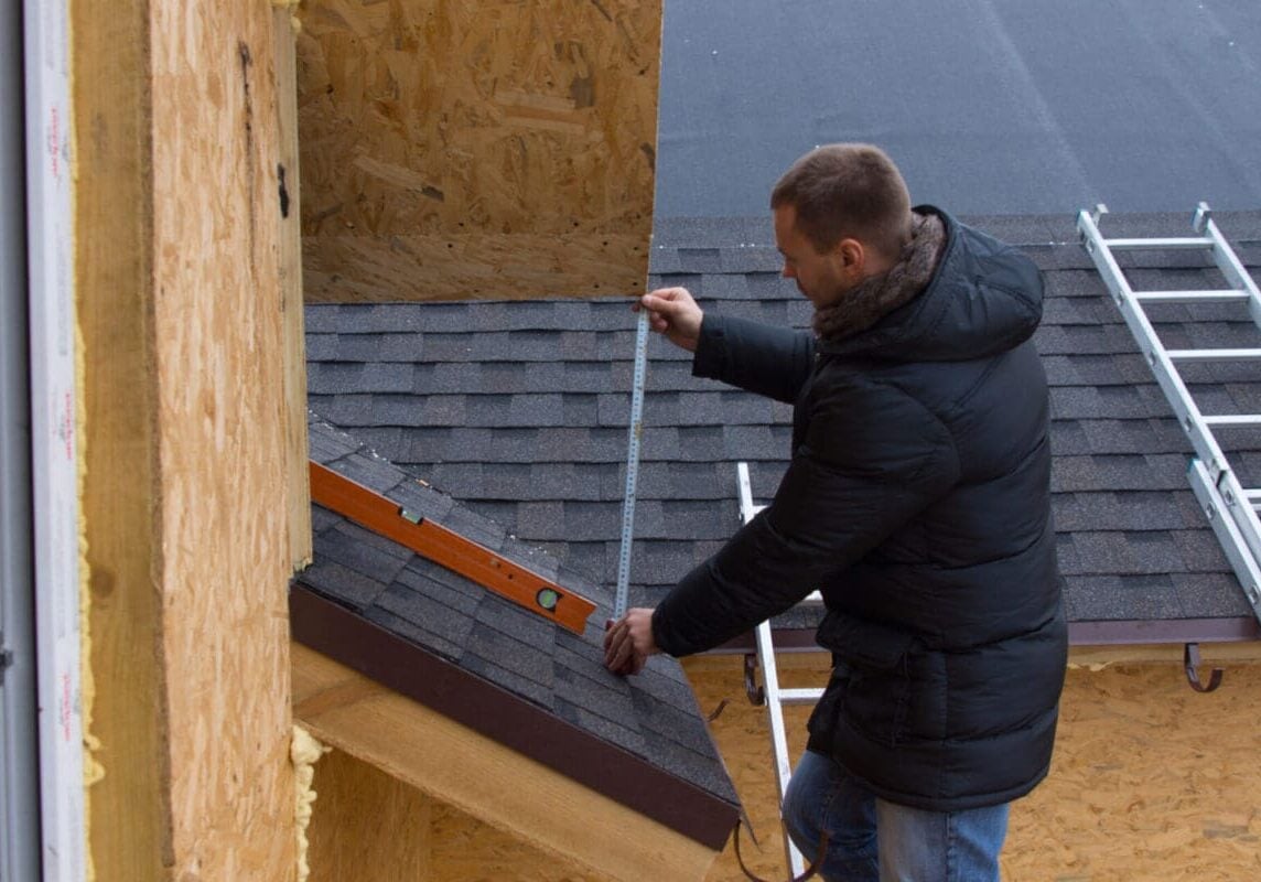 low slope roof pitch Roofer measuring tiles on a new house with a tape measure as he stands on a ladder while installing the roof