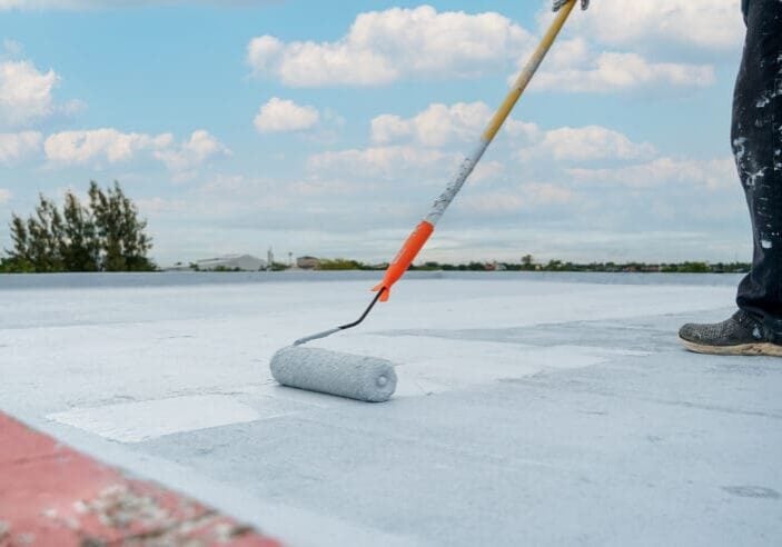 commercial roof coating cost worker applying coat using paint roller