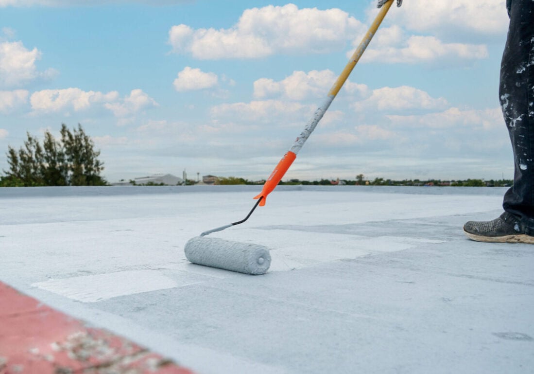 commercial roof coating cost worker applying coat using paint roller