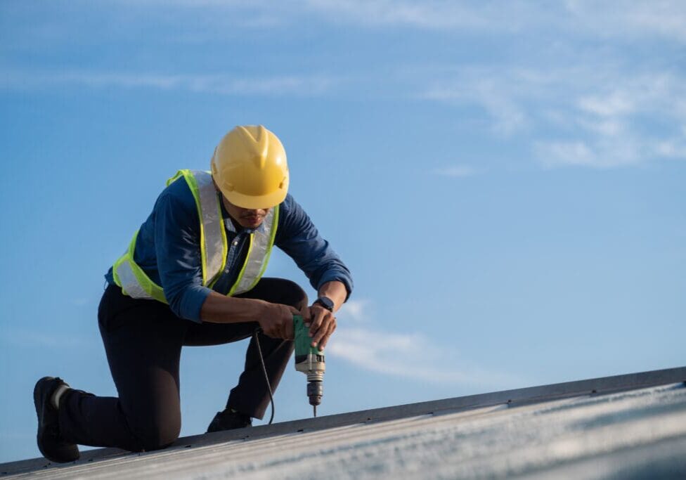 Worker repairing the roof on a construction site. Electric drill used on roof, Roof construction concept.