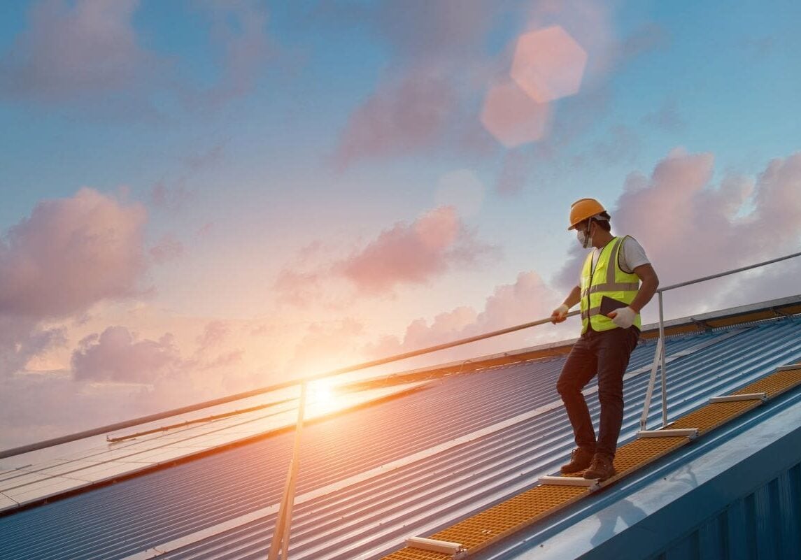 commercial roof preventative maintenance worker walking on top of metallic roof with rope